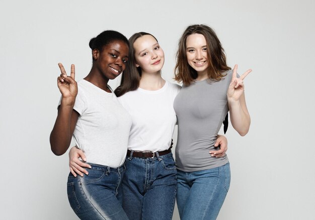 Retrato de jóvenes mujeres multirraciales de pie juntas y sonriendo a la cámara aislada sobre fondo blanco.