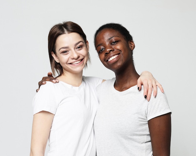 Retrato de jóvenes mujeres multirraciales de pie juntas y sonriendo a la cámara aislada sobre fondo blanco.