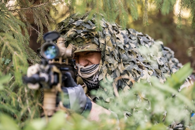 Retrato de jóvenes soldados serios en trajes de camuflaje de pie con arma contra árboles forestales