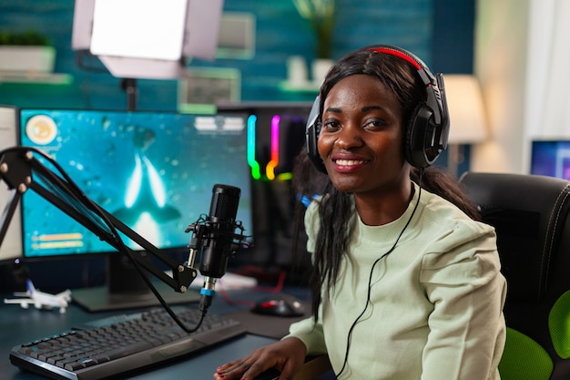 Retrato de jugador africano streamer profesional e mirando a la cámara. Transmisión de videojuegos virales para divertirse usando auriculares y teclado para el campeonato en línea.