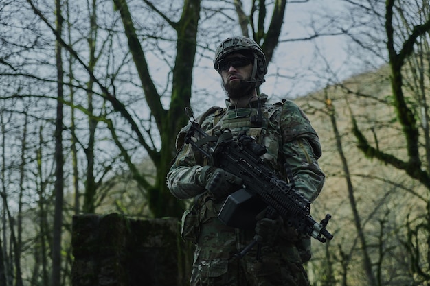 Retrato de jugador de airsoft en equipo profesional con ametralladora en el bosque. Soldado con armas en guerra