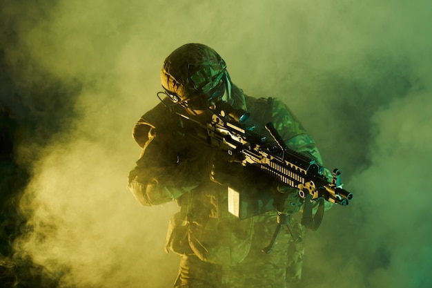 Retrato de jugador de airsoft en equipo profesional con ametralladora en edificio abandonado en ruinas. Soldado con armas en guerra en humo y niebla.