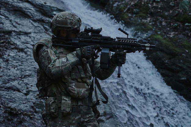 Retrato de jugador de airsoft en equipo profesional en casco apuntando a la víctima con pistola en el bosque. Soldado con armas en guerra