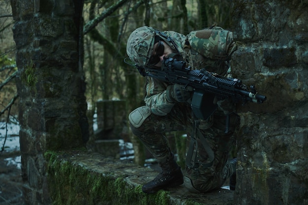 Retrato de jugador de airsoft en equipo profesional en casco apuntando a la víctima con pistola en el bosque. Soldado con armas en guerra