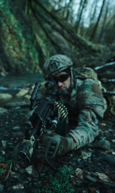 Retrato de jugador de airsoft en equipo profesional en casco apuntando a la víctima con pistola en el bosque. Soldado con armas en guerra