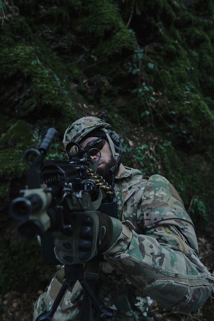 Retrato de jugador de airsoft en equipo profesional en casco apuntando a la víctima con pistola en el bosque. Soldado con armas en guerra