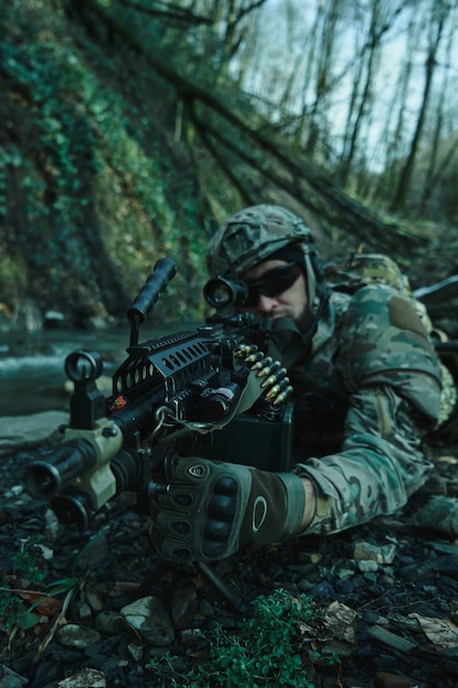 Foto retrato de jugador de airsoft en equipo profesional en casco apuntando a la víctima con pistola en el bosque. soldado con armas en guerra