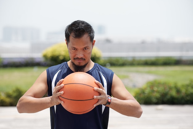 Retrato de jugador de baloncesto determinado apretando la bola y mirando a la cámara