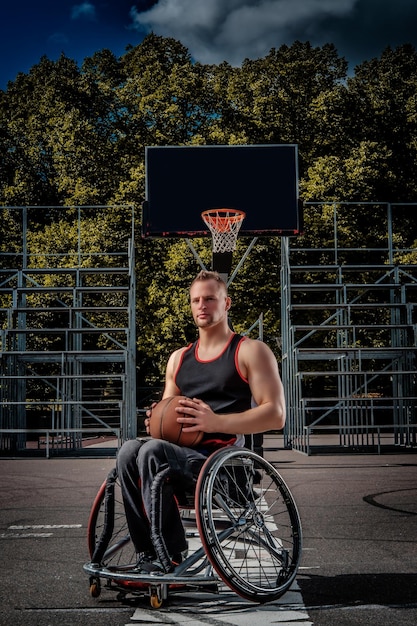 Retrato de un jugador de baloncesto discapacitado en silla de ruedas en un terreno de juego abierto.