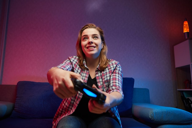 Retrato de jugador loco y juguetón, niña disfrutando de jugar videojuegos en el interior sentado en el sofá, sosteniendo la consola Gamepad en las manos. Descansando en casa, que tengas un gran fin de semana