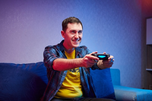 Retrato de jugador loco juguetón, niño disfrutando de jugar videojuegos en el interior sentado en el sofá, sosteniendo la consola Gamepad en las manos. Descansando en casa, que tengas un gran fin de semana