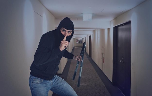 Retrato de un ladrón sosteniendo una herramienta de trabajo de pie en el pasillo
