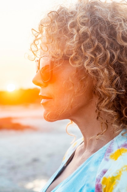 Retrato lateral de mulher linda e encaracolada com o pôr-do-sol em fundo em atividade de lazer ao ar livre sozinha Pessoas femininas atraentes de cabelo longo adultos em contemplação Pessoas estilo de vida Senhora bonita