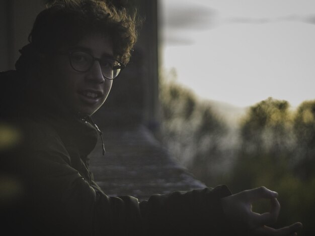 Retrato lateral de um jovem apoiado em um corrimão durante o pôr-do-sol