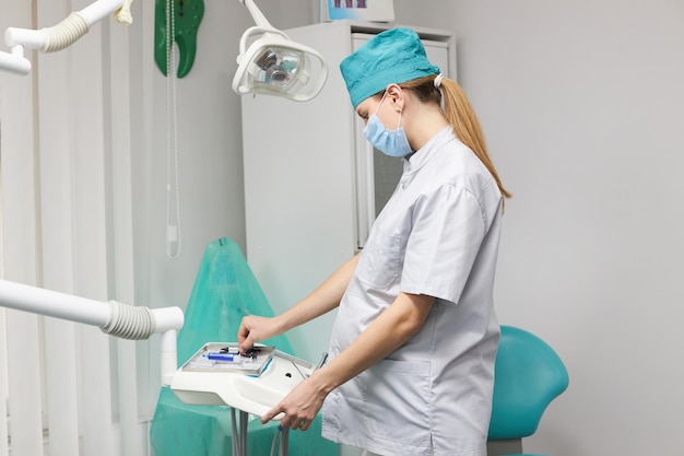 Retrato lateral de uma assistente de dentista grávida preparando o local de trabalho no consultório odontológico