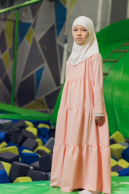 Retrato lateral de uma menina muçulmana usando um hijab. Conceito de roupa muçulmana para crianças. no contexto do playground.