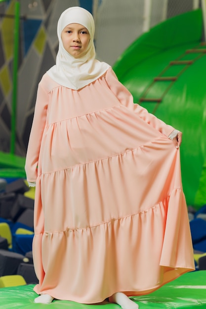 Retrato lateral de uma menina muçulmana usando um hijab. Conceito de roupa muçulmana para crianças. no contexto do playground.