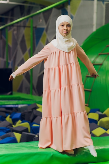 Retrato lateral de uma menina muçulmana usando um hijab. Conceito de roupa muçulmana para crianças. no contexto do playground.