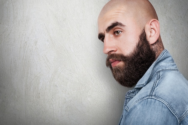 Un retrato lateral con espacio de copia del hipster calvo de moda que tiene un tatuaje en el cuello, gruesas cejas negras y barba