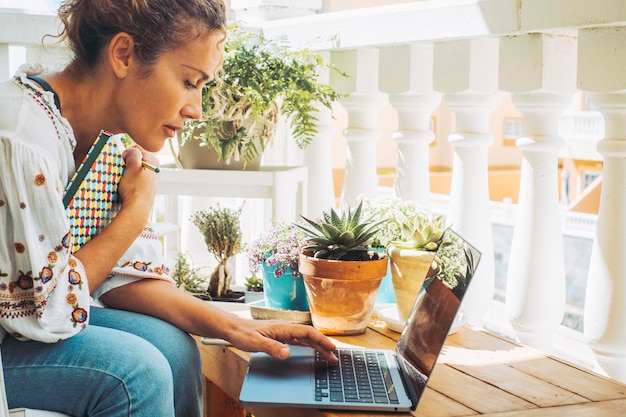 Retrato lateral de una mujer de negocios seria que trabaja desde casa en una terraza al aire libre usando una computadora portátil Conexión inalámbrica de personas y computadoras Concepto de trabajo en línea y estilo de vida de trabajo digital Trabajo inteligente femenino