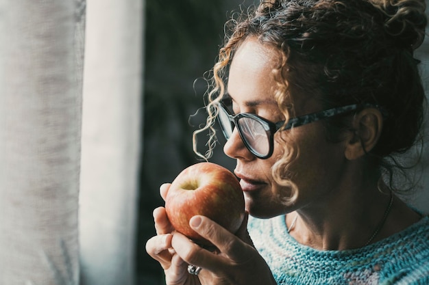 Retrato lateral de una mujer sosteniendo una manzana y mirando por la ventana en casa Concepto de estilo de vida de alimentos saludables y frutas Mujeres pensativas en actividades de ocio interior Señora de mediana edad