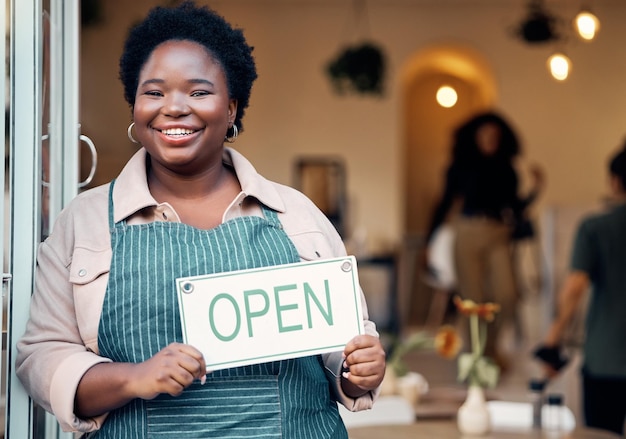 Retrato de letrero abierto y mujer negra en el inicio de una pequeña empresa para comprar servicio al cliente y éxito minorista Gerente de jefe o persona que sostiene el tablero para recibir la bienvenida en la nueva tienda con una sonrisa en la puerta