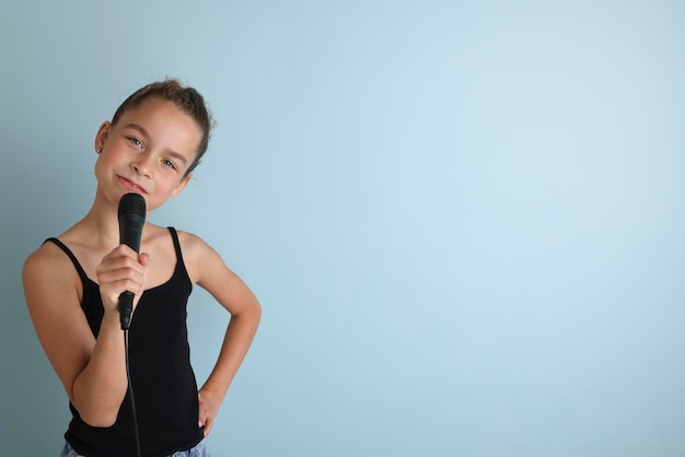 Retrato de una linda adolescente cantando con micrófono Adolescente con camiseta negra sobre un fondo azul aislado Karaoke para niños Entretenimiento en el hogar para niños Cantante cantando con micrófono