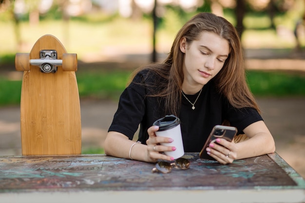 Retrato de una linda adolescente con una patineta sentada y descansando en el banco al aire libre del parque de patinaje