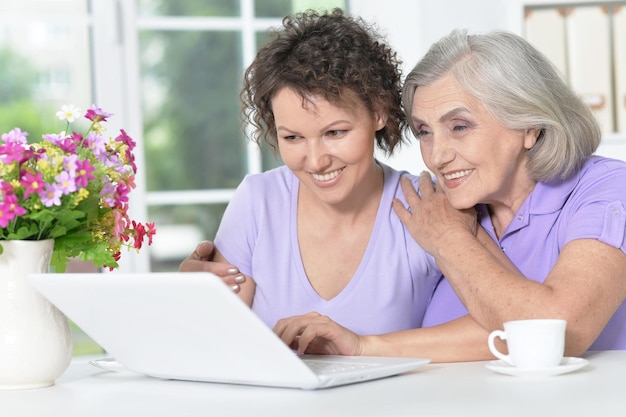 Retrato de una linda anciana con una hija usando una laptop