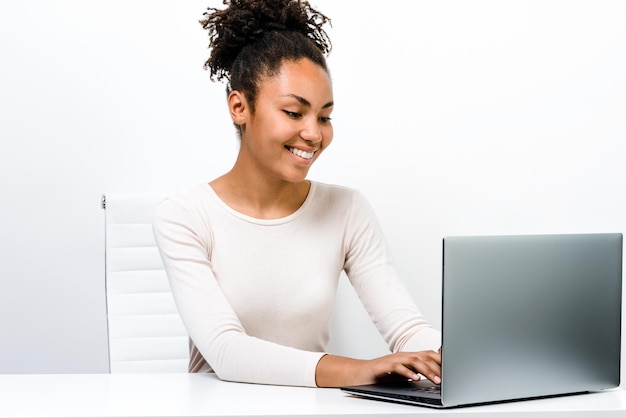 Retrato de una linda y atractiva chica multirracial sentada y usando una laptop para comercio electrónico aislada de fondo blanco Ella tiene una sonrisa de placer