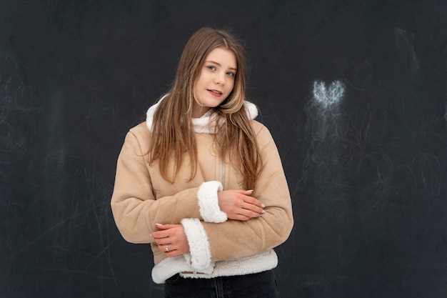 Retrato de una linda chica con un abrigo corto de piel de oveja beige con piel sobre fondo negro Ropa cómoda de invierno en modelo