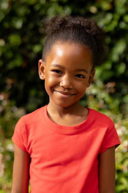 Retrato de una linda chica afroamericana sonriente parada contra plantas al aire libre