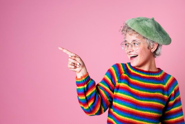 Retrato de una linda chica alegre con gafas apuntando hacia los lados en un fondo rosa