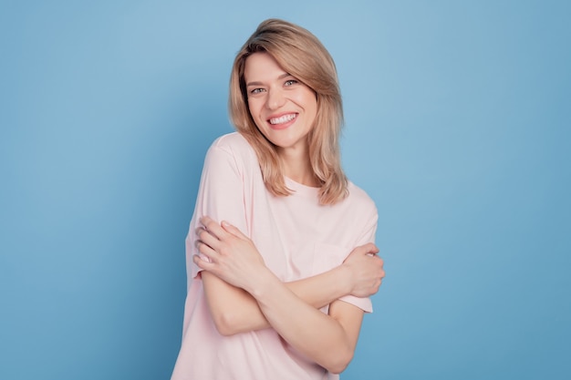 Retrato de linda chica atractiva abrazo a sí misma con dientes sonrisa radiante sobre fondo azul.