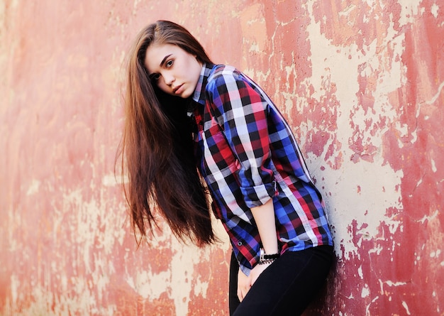 Retrato de linda chica morena joven en camisa a cuadros en la superficie de la pared de grunge rojo. Copia espacio, espacio para texto