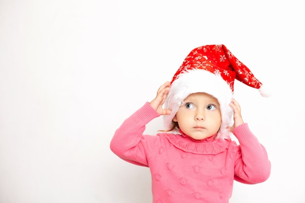 Retrato de una linda chica de ojos azules con una gorra navideña y un jersey rosa Fondo blanco