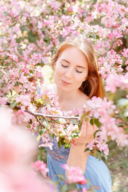 Retrato de una linda chica pelirroja cerca de un árbol floreciente con flores rosadas en el jardín parque floreciente de la manzana en primavera