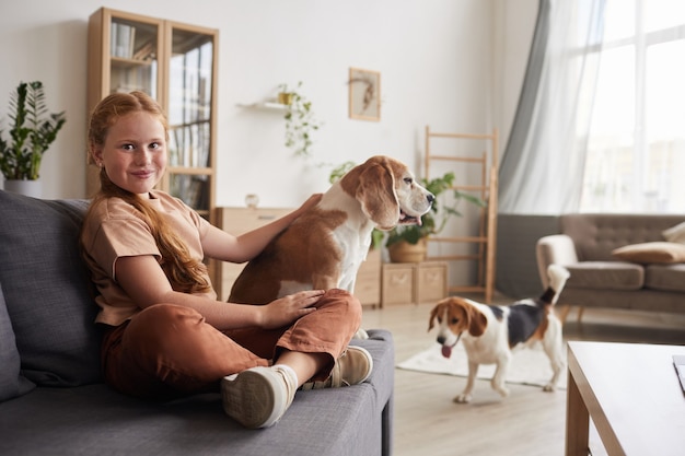 Foto retrato de linda chica pelirroja jugando con perros sentado con las piernas cruzadas en el sofá en casa