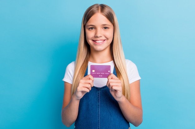 Foto retrato de linda chica de pelo largo rubio agradable mostrando ropa casual con tarjeta de crédito aislado sobre fondo de color azul pastel