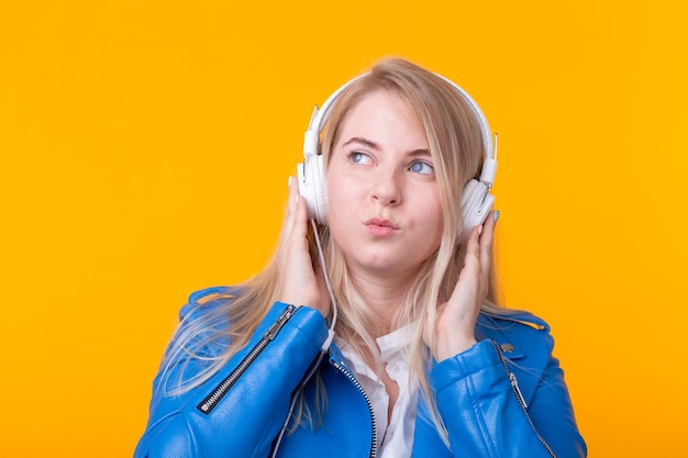 Retrato de linda chica rubia joven positiva escuchando música favorita en auriculares en azul