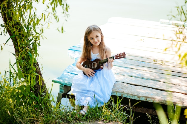 Retrato de una linda chica sentada ouddoor con ukelele