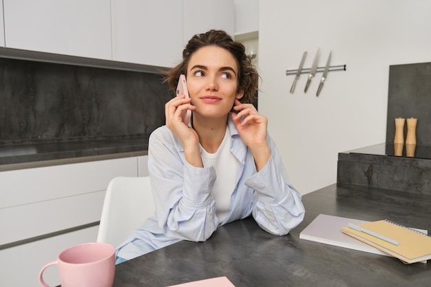 Retrato de una linda chica sonriente habla por teléfono móvil se sienta en casa y llama a alguien con un teléfono inteligente