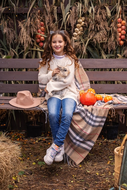 Retrato de una linda chica sosteniendo un conejo mullido en el otoño en el patio