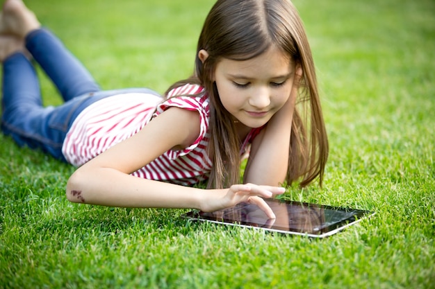Retrato de linda chica con tableta digital en el parque sobre el césped