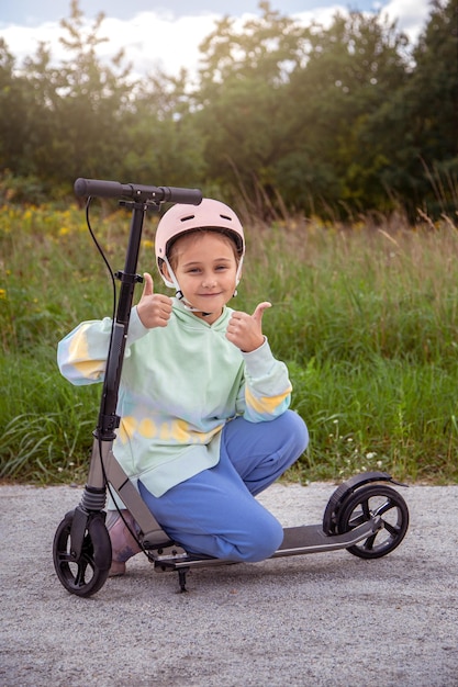 Retrato de una linda colegiala caucásica con casco que disfruta divirtiéndose montando scooter en el parque asfaltado de la calle trackxAin al aire libre en un día soleado Actividades deportivas saludables para niños afuera