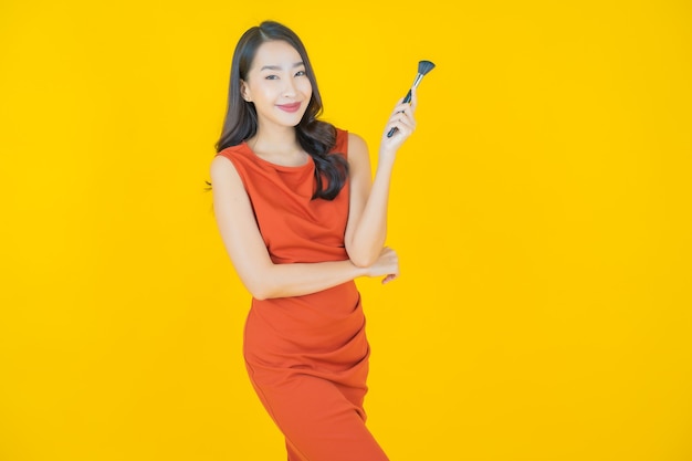 Retrato linda jovem asiática com maquiagem escova cosmética em amarelo