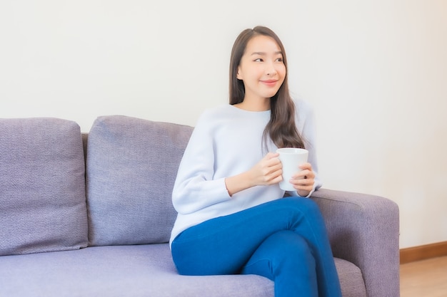 Retrato linda jovem asiática com uma xícara de café no sofá no interior da sala de estar