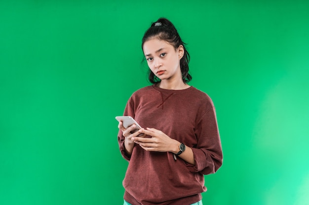 Retrato linda jovem asiática segurando um telefone enquanto olha para a câmera sobre um fundo verde