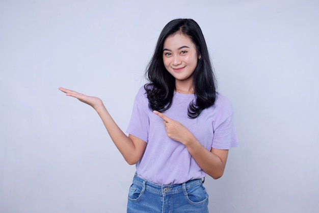 Retrato linda jovem asiática sorrindo com ação, mostrando algo na parede branca