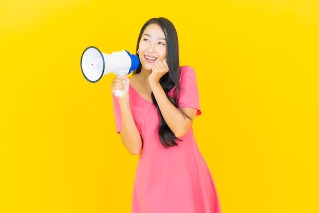 Retrato linda jovem asiática sorrindo com megafone na parede amarela